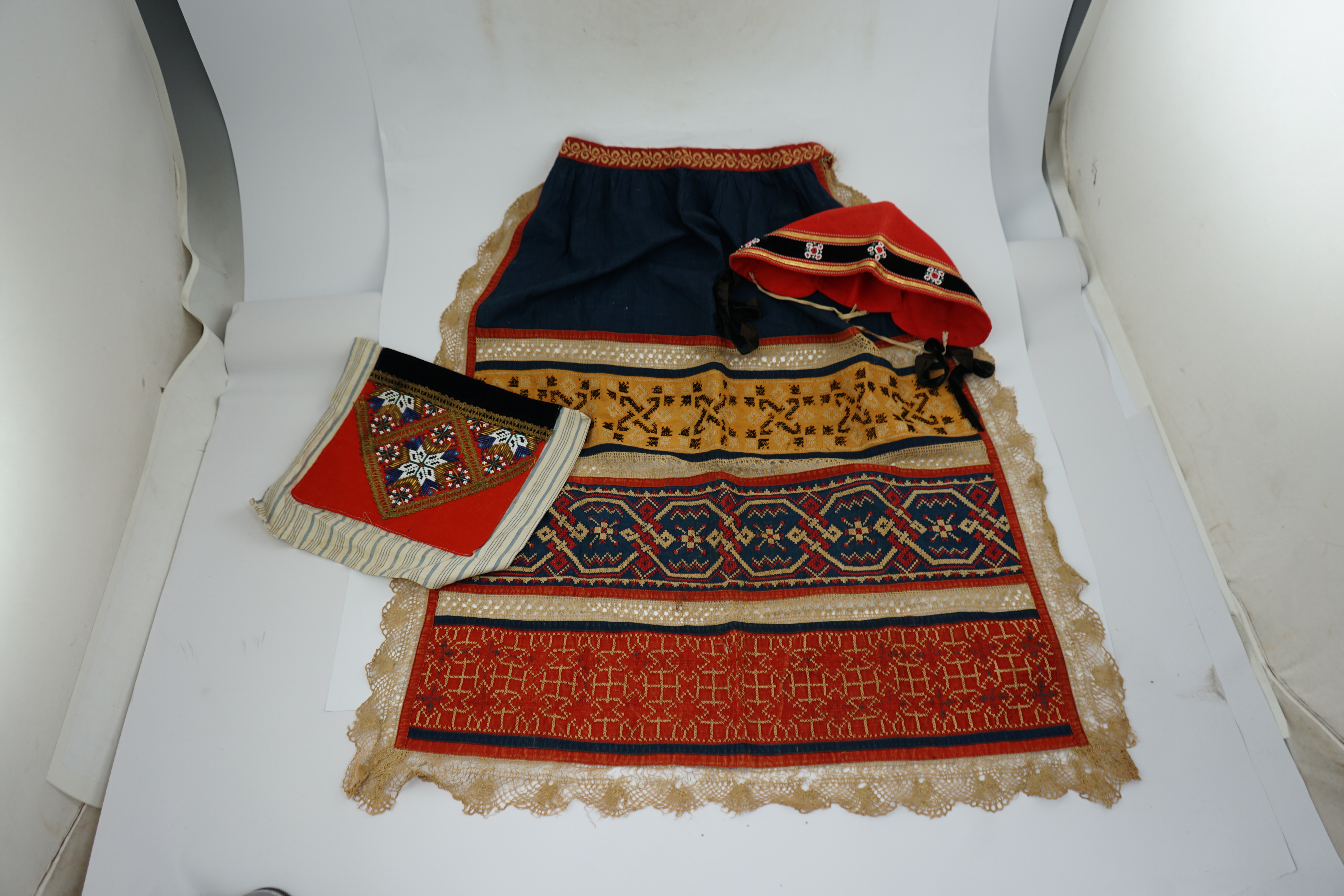 An Eastern European, possibly Ukrainian, apron and a Norwegian beaded bodice front, with child’s cap, the apron worked in rows of coloured cotton, embroidered with cross stitch patterns and lace insertions, the bodice, b